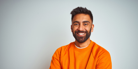 Young indian man wearing orange sweater and smiling