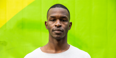 Man with neutral look standing in front of camera wearing a white t-shirt on a bright green background