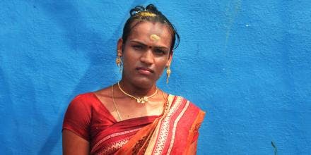 A transgender woman in red sari standing against a blue wall