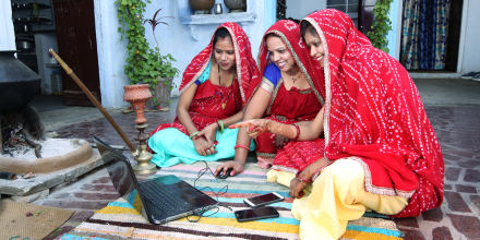 Traditional Indian young married women working in traditional kitchen on laptop