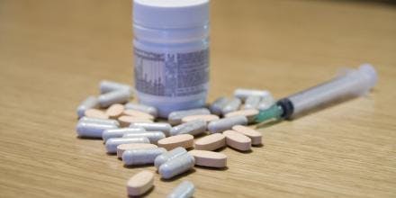 Some pills, bottle of pills and syringe on a table