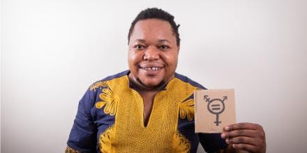 Studio portrait of an African trans person holding a cardboard with the trans symbol