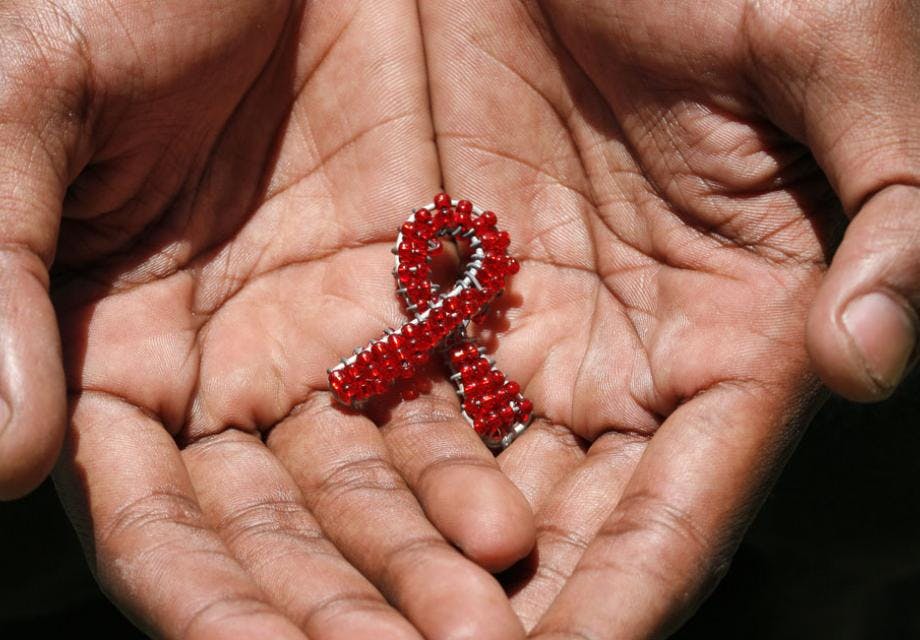 A close up of hands holding a beaded metal AIDS ribbon 