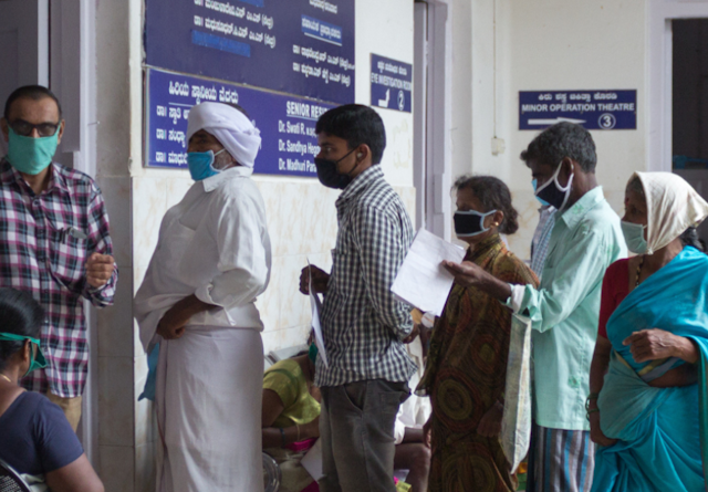 People wearing masks wait in line at a clinic in India