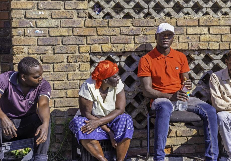 Three African men and one woman sitting on the sidewalk 