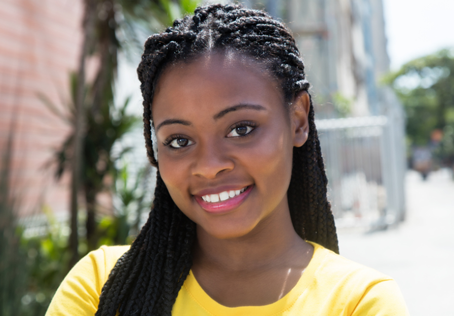 Laughing african american woman in a yellow shirt in the city with streets, trees and buildings in the background