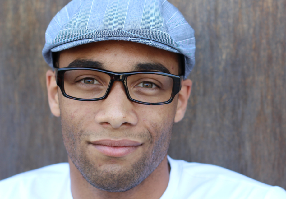 Young man wearing glasses and a hat smiling at the camera