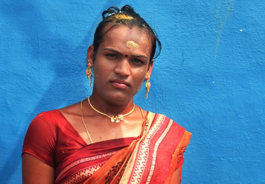 A transgender woman in red sari standing against a blue wall