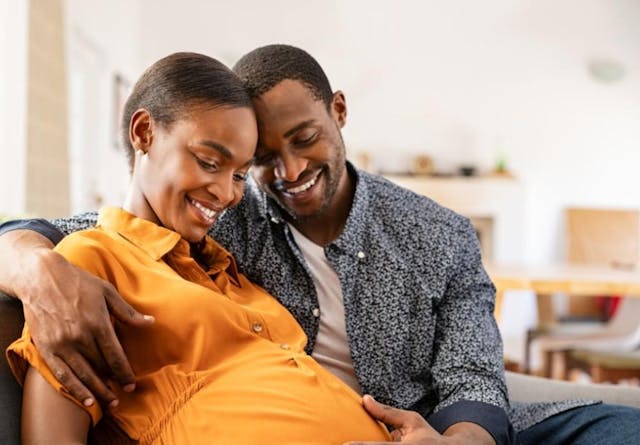 Black expectant parents sitting on sofa dreaming about their baby