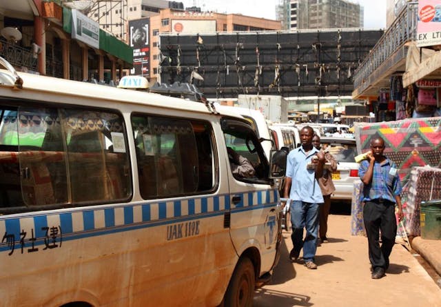 Taxis line up on a street in Uganda, men walk by