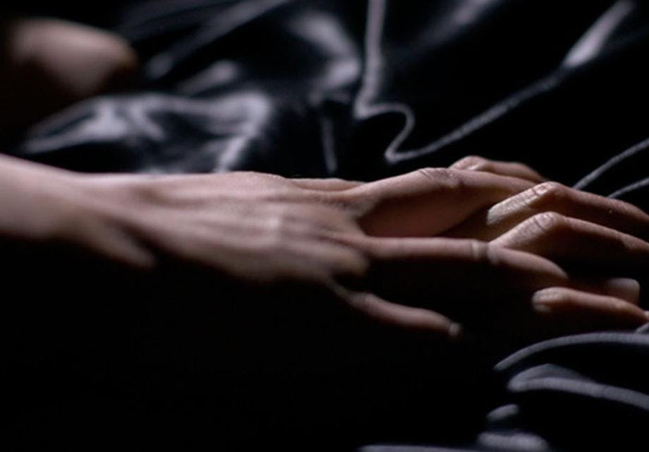Two hands grasping each other on top of a black bed sheet