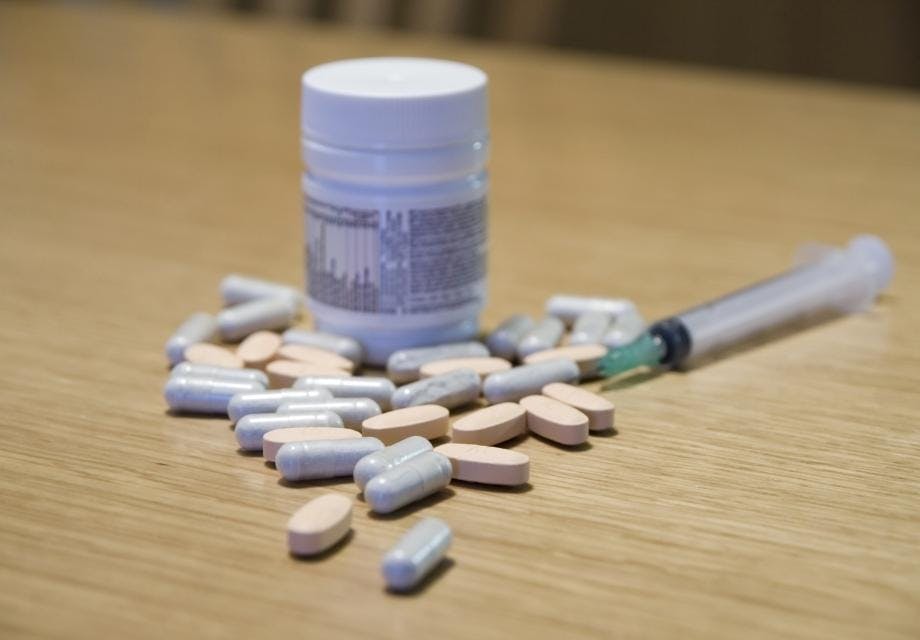 Some pills, bottle of pills and syringe on a table