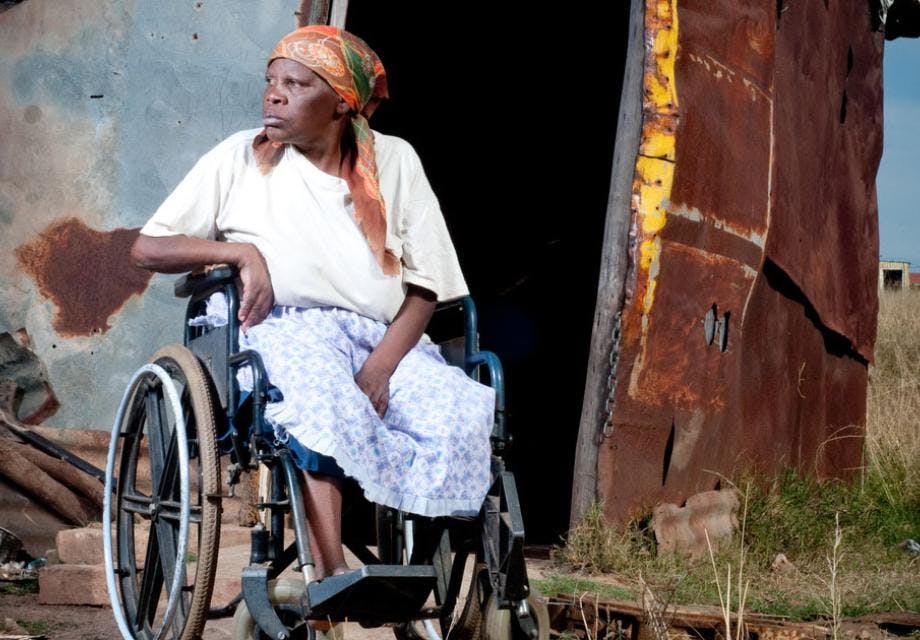 A woman sits in a wheelchair outside rural house in Africa