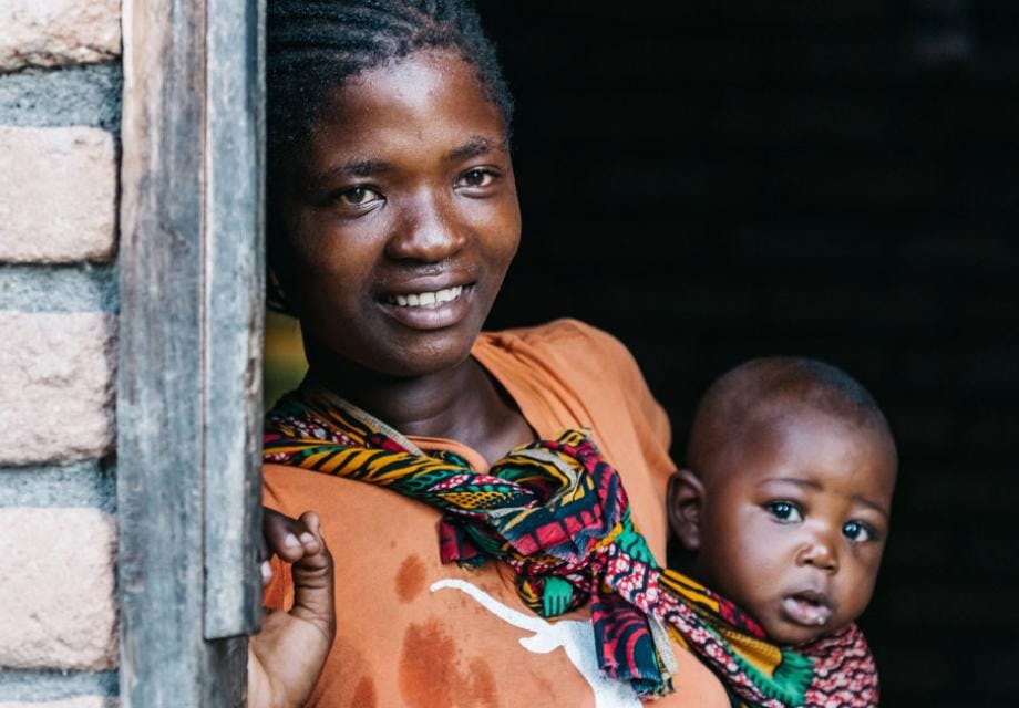 A young African mother looks out of the door with her baby
