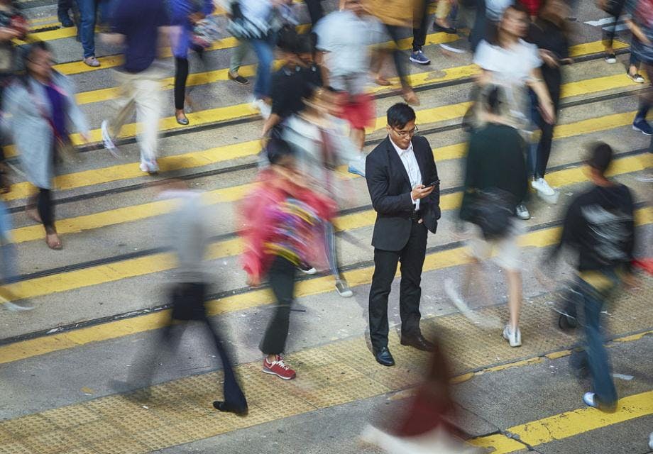 A chinese man standing in the street looking at his phone amidst a crowd