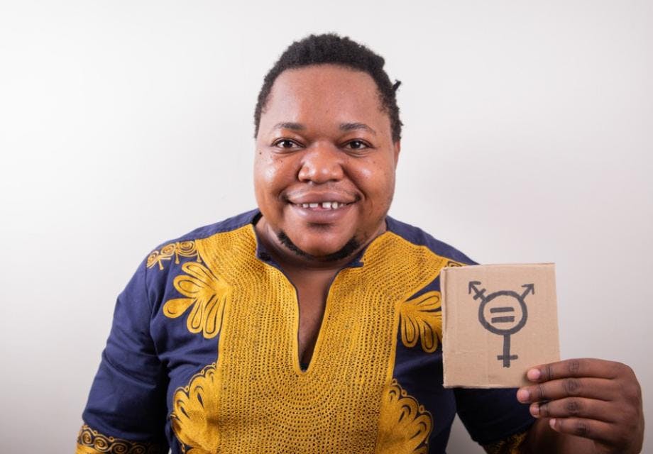 Studio portrait of an African trans person holding a cardboard with the trans symbol