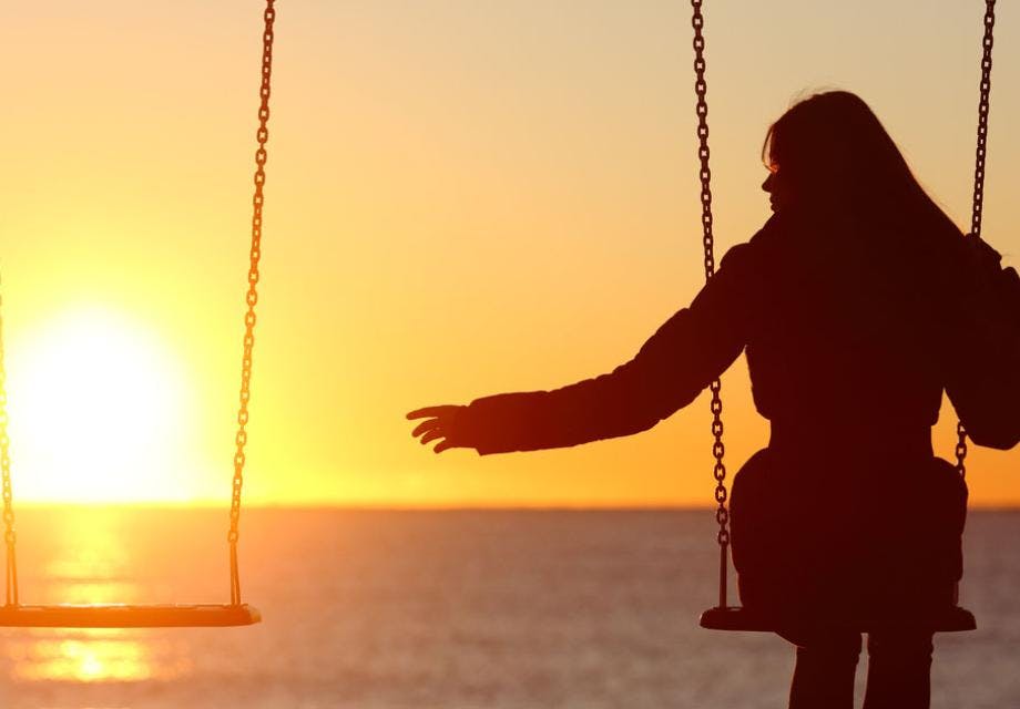 A woman sitting alone on a swing with a sunset in the background