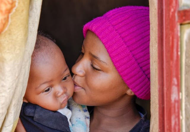 village life, happy african woman kissing her child in the window